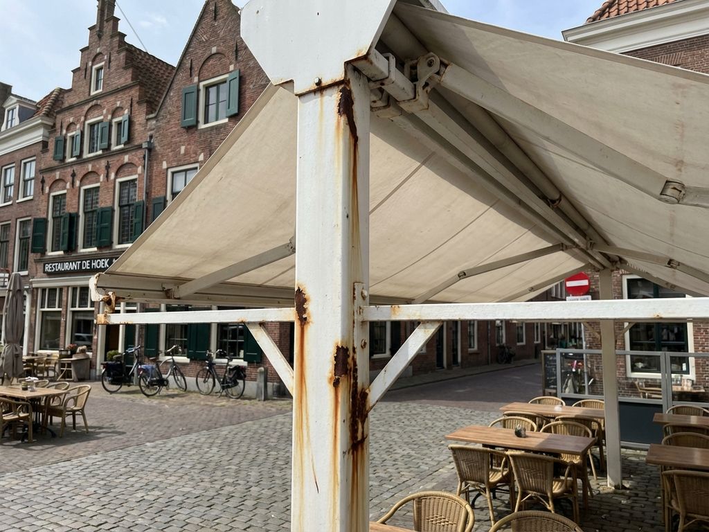 Wit luifelframe met roeststrepen op Nederlands restaurantterras met bakstenen gebouwen op achtergrond