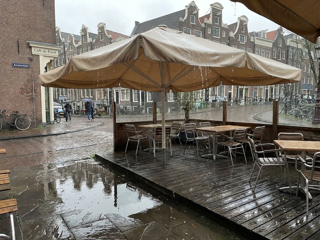 Natte beige parasol op Nederlands terras met water druppelend door stof na regenbui