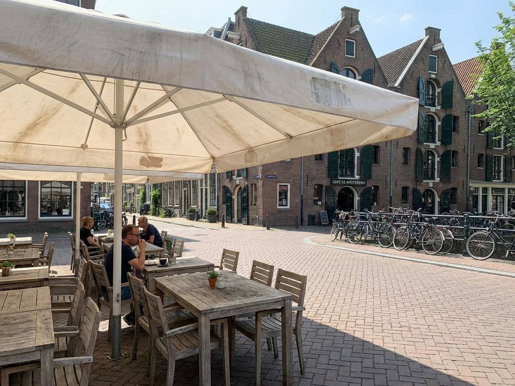 Verweerde parasol op Nederlands restaurantterras met houten meubilair en traditionele architectuur op achtergrond