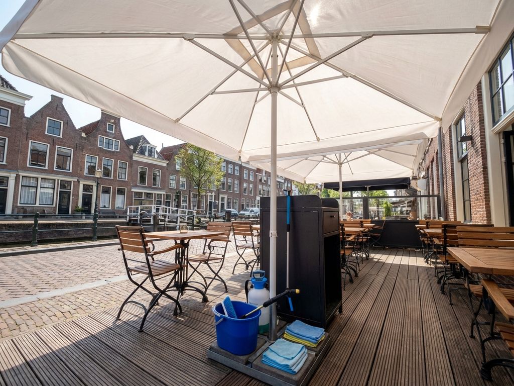 Witte parasol op Nederlands restaurant terras met professionele schoonmaakapparatuur en traditionele bakstenen gebouwen