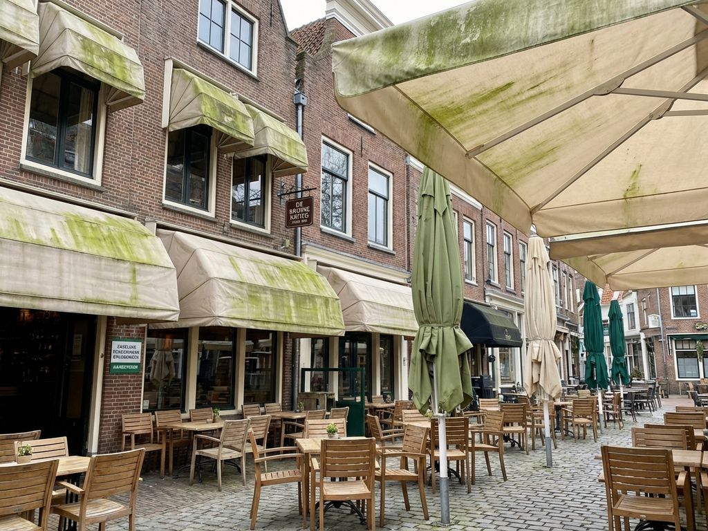Nederlandse restaurant terras met parasols en luifels met groene algen groei, typische bakstenen gebouwen op achtergrond
