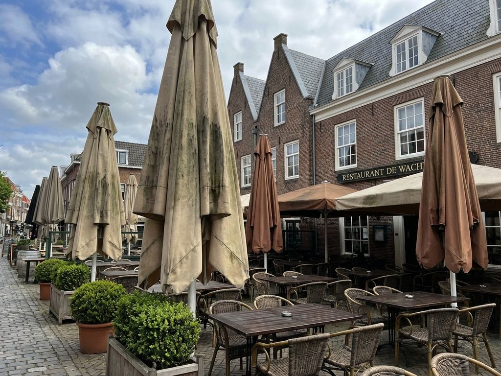Restaurantterras met verweerde parasols met vlekken en beschadigingen, Nederlandse bakstenen gebouwen op achtergrond