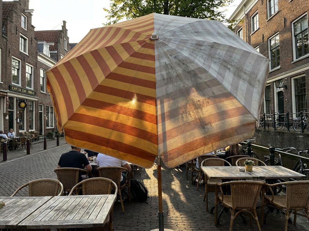 Grote parasol op Nederlands restaurantterras toont verschil tussen schone en verweerde delen in zonlicht
