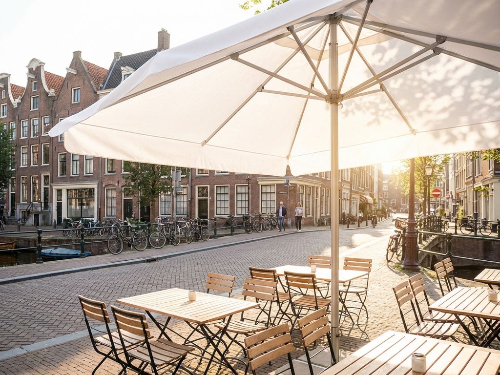 Schone witte parasol op Nederlands restaurantterras met lege tafels en karakteristieke bakstenen gebouwen op achtergrond