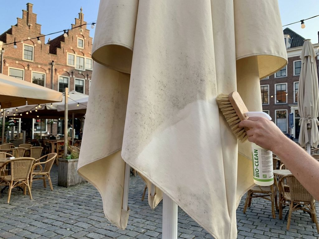 Grote parasol op Nederlands restaurantterras wordt natuurlijk gereinigd, bakstenen gebouwen op achtergrond