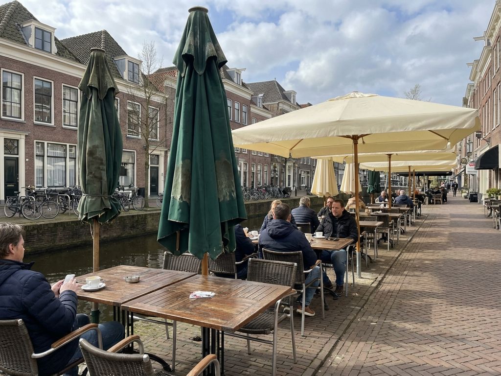 Nederlandse restaurantterras met parasols in verschillende staat van onderhoud bij kanalenzijde architectuur