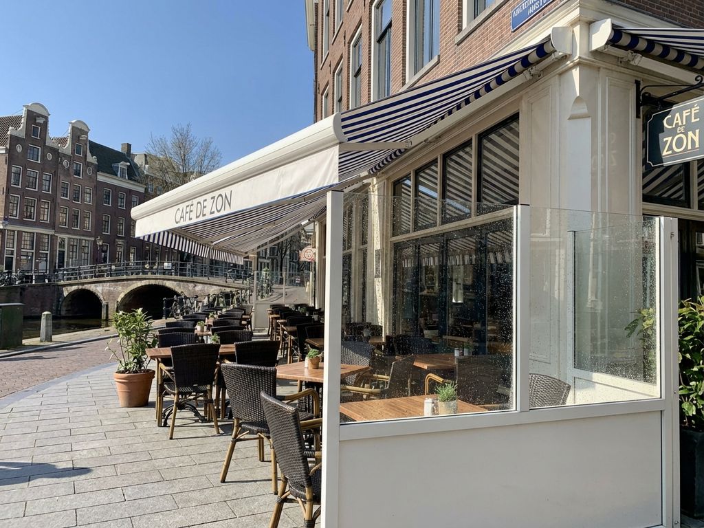 Schoon Nederlands restaurantterras met gestreepte luifels en glazen windschermen in zonlicht langs grachten
