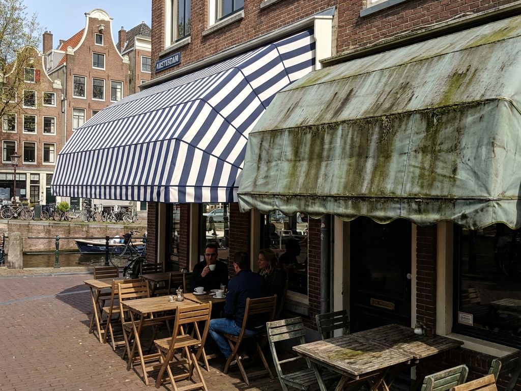 Nederlandse restaurantterras met schone en vuile luifels naast elkaar, toont onderhoudsverschil bij historische bakstenen gebouwen