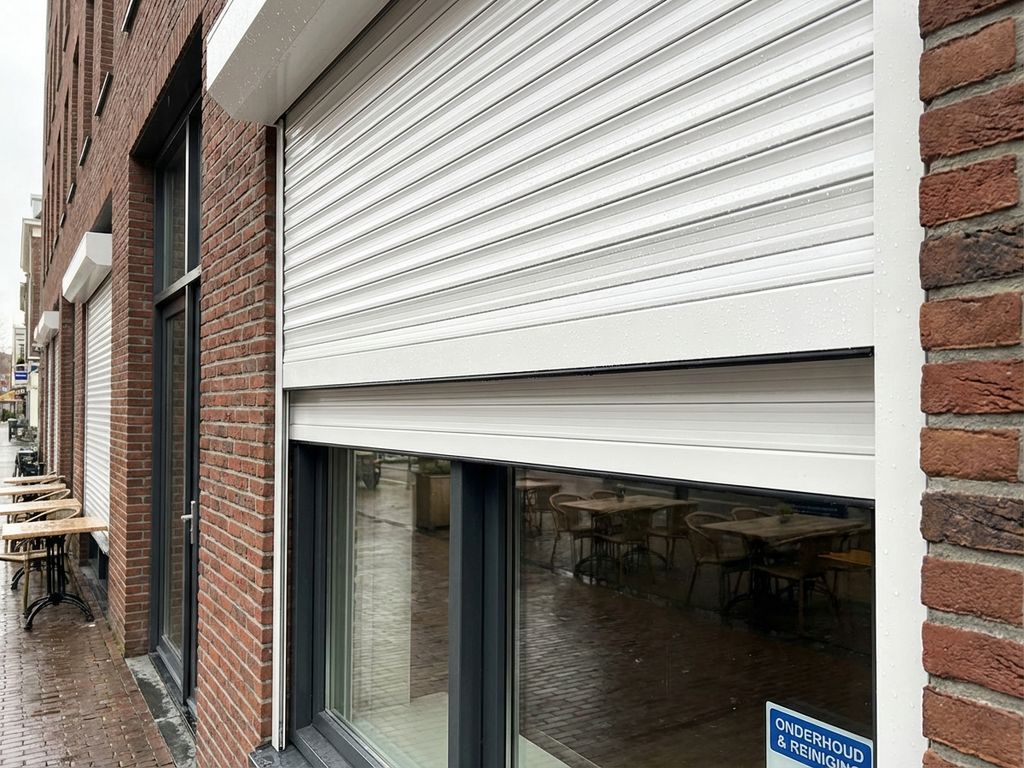 Schone witte rolluiken op Nederlandse bedrijfsgevel met bakstenen architectuur, gedeeltelijk geopend in daglicht