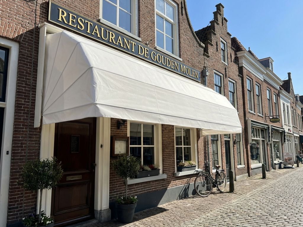 Schone witte luifel boven Nederlandse restaurant ingang met traditionele bakstenen architectuur en kasseien