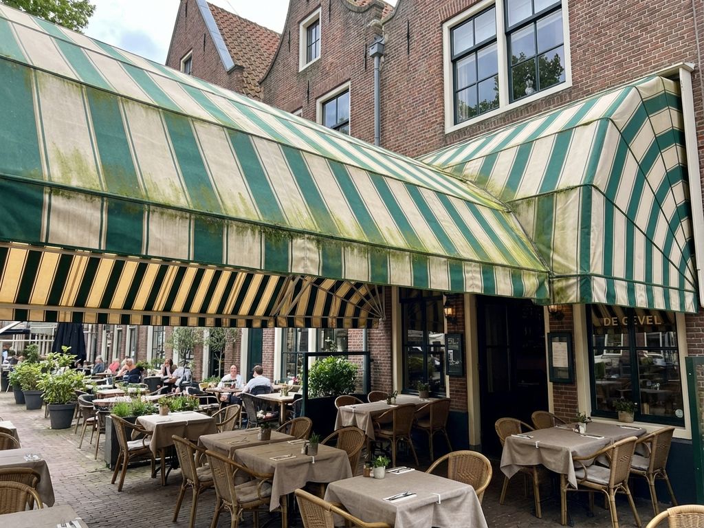 Nederlandse restaurantterras met gestreepte luifel met lichte algengroei, bakstenen gebouwen op achtergrond