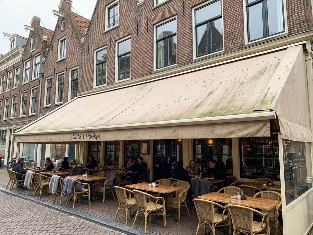 Beige luifel met donkere schimmelvlekken boven restaurantterras met Nederlandse bakstenen gebouwen op achtergrond