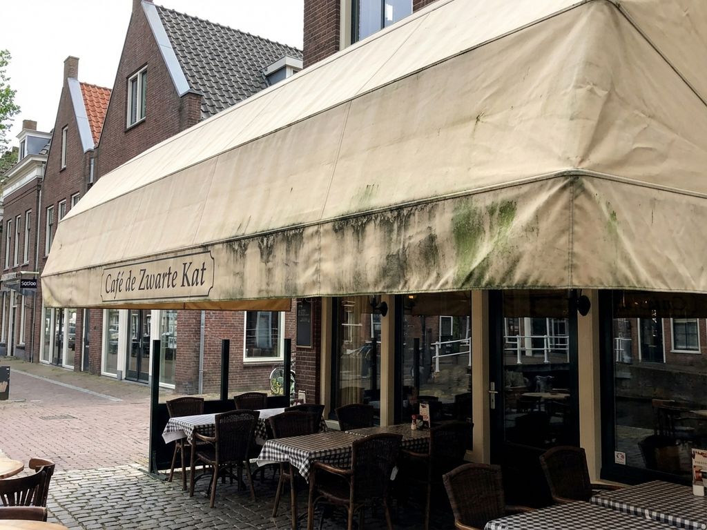 Nederlandse restaurantterras met vervuild zonnescherm dat donkere vlekken en verwering toont aan de onderrand