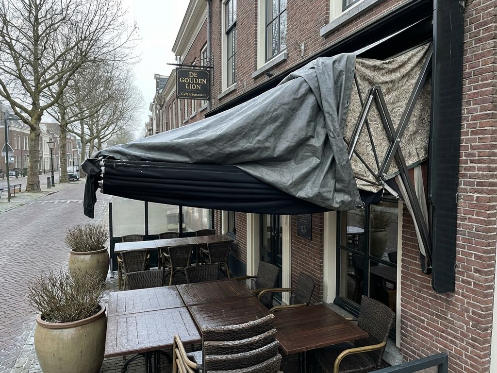 Terras van Nederlands restaurant in winter met ingetrokken zonwering en beschermhoes, buitenmeubilair en kale bomen