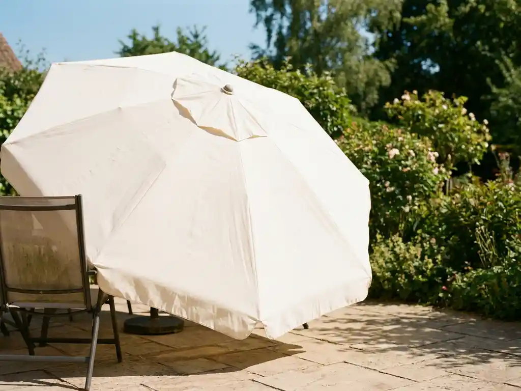 Grote crèmekleurige parasol volledig geopend en luchten op zonnig terras, schone stof glanst in natuurlijk middaglicht met groene tuin op achtergrond.
