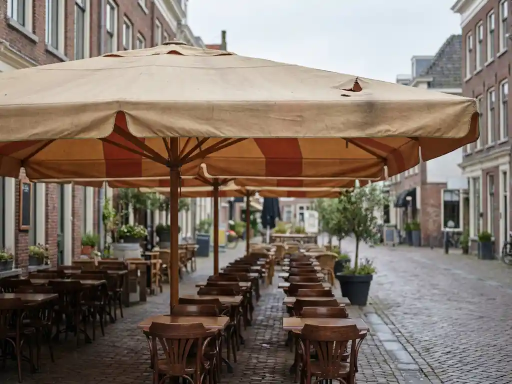 Beschadigde terrasoverstek met kleine scheur boven een Nederlands restaurantterras met houten bistrostoelen en kasseienstraat op de achtergrond.