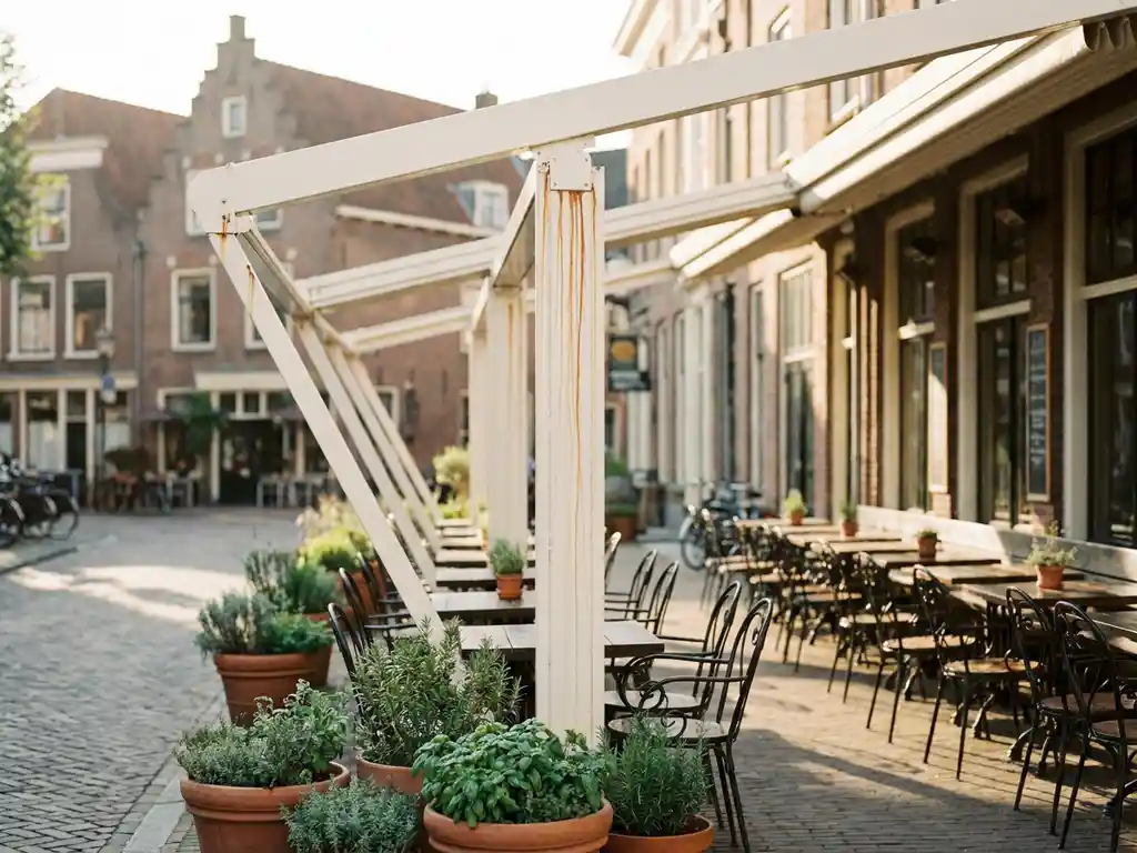 Verroest wit zonnescherm op terras van Nederlands restaurant met smeedijzeren stoelen en kruiden op de achtergrond.
