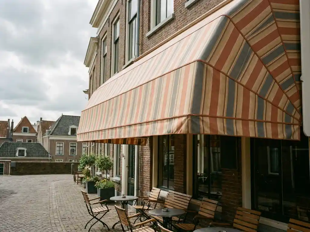 Schoongemaakt gestreept terrasscherm boven Nederlands restaurantterras met stoelen en ronde tafeltjes in zacht middagslicht.