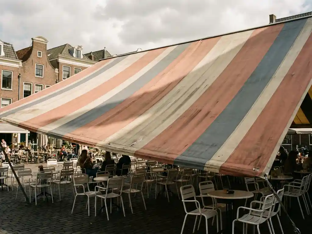 Vervaagd terrasoverkapping boven een Nederlands restaurantterras met witte stoelen en ronde tafeltjes in warm middagzonlicht.