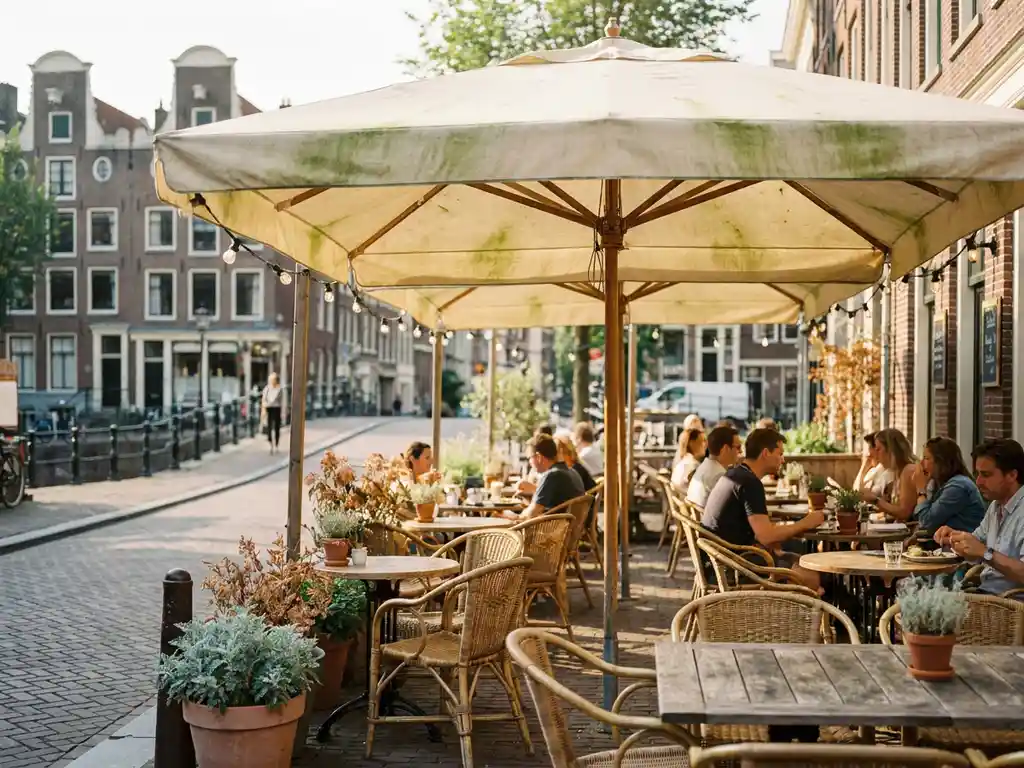 Terrasparasol met groene algevlekken op een Nederlands terras, met bistrostoelen en kanaalbebouwing op de achtergrond.