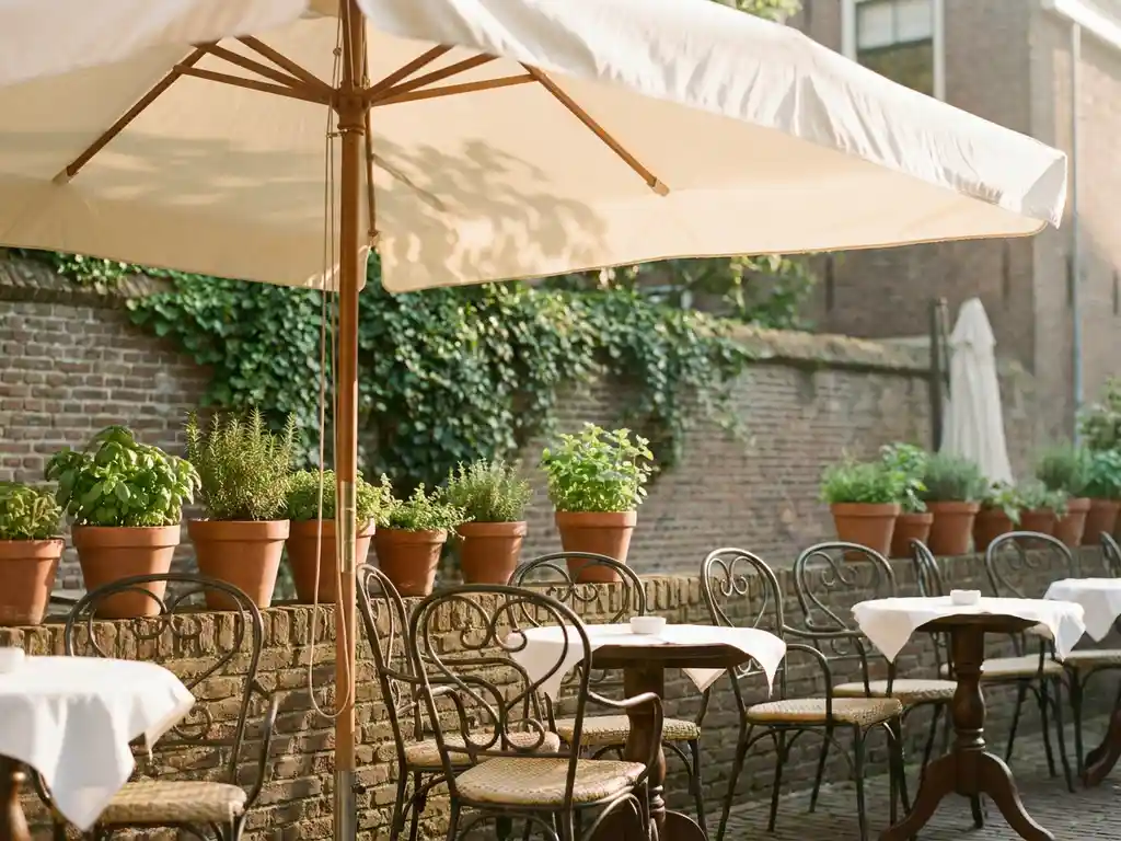 Groot tuinparasol met crèmekleurig doek op zonnig terras van Nederlands restaurant met bistrostoelen en kruidenpotten.