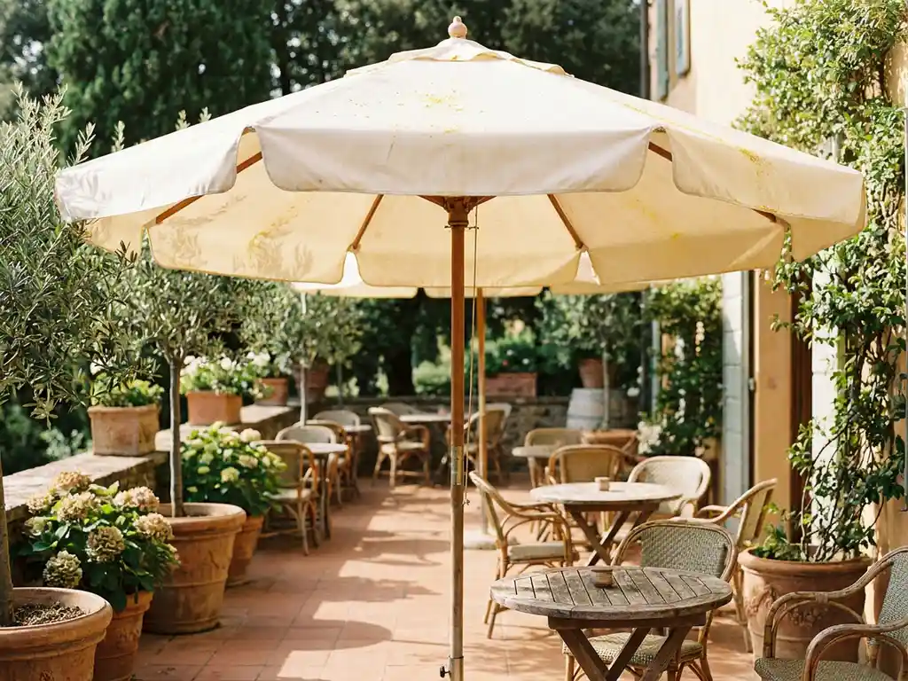 Groot crèmekleurig terrasparasol op een zonnig Nederlands restaurantterras met bistrostoelen, terracotta tegels en weelderig groen.