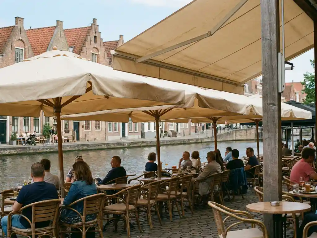 Rij zandkleurige parasols boven een terras aan een Amsterdamse gracht, met houten bistrostoelen en ronde tafeltjes in zacht daglicht.