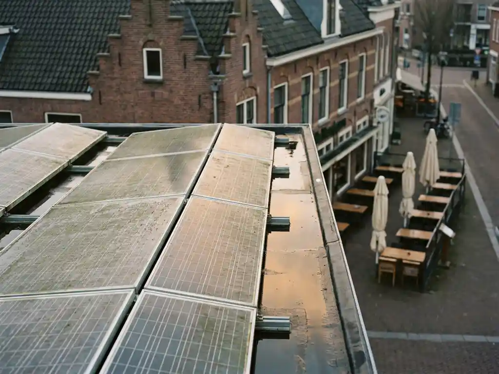 Licht bestoft zonnepanelensysteem op plat commercieel dak in Nederland, met traditioneel bakstenen gebouw en restaurantterras op de achtergrond.